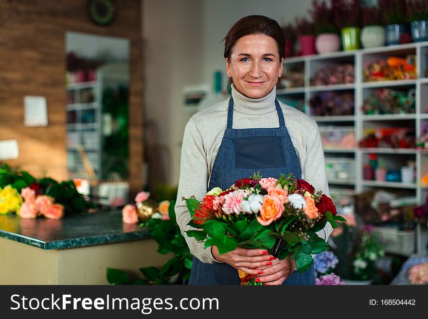 A cute flower girl in a blue apron holds a beautiful composition of flowers and looks at the camera with a smile. A cute flower girl in a blue apron holds a beautiful composition of flowers and looks at the camera with a smile.