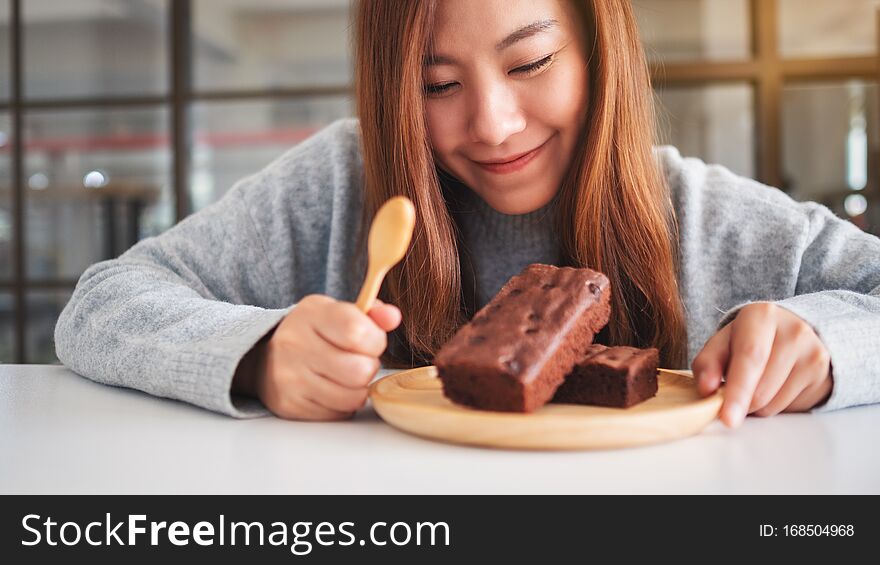 A beautiful asian woman looking and eating delicious brownie cake in wooden plate