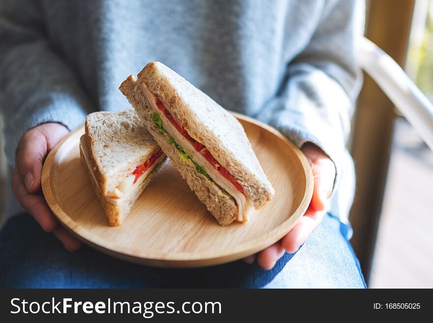 A woman holding and serving two pieces of whole wheat sandwich