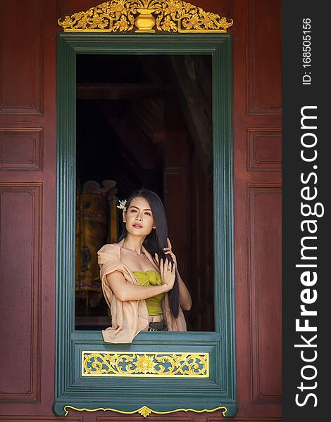 Woman wearing Thai costume combing hair in window. Asian girl wearing Thai traditional dress hand holding hair on window. looking