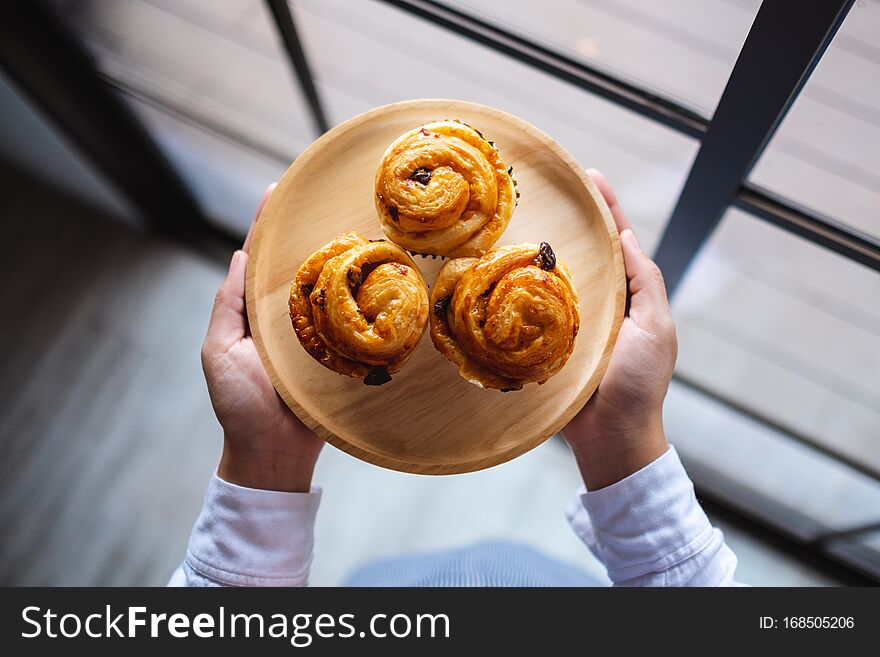 Top view image of a waitress holding a wooden plate of raisin danish