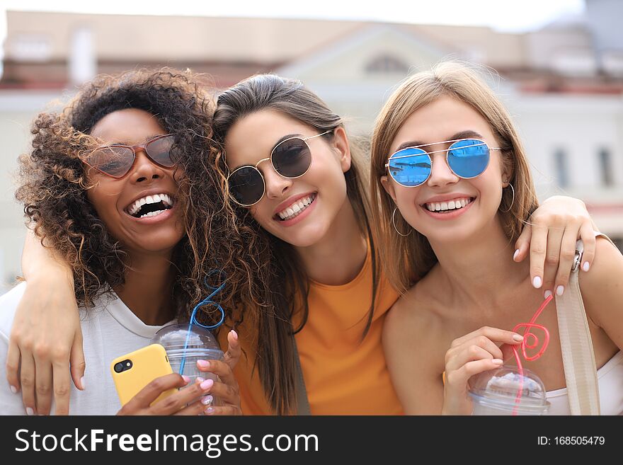 Three trendy cool hipster girls, friends drink cocktail in urban city background