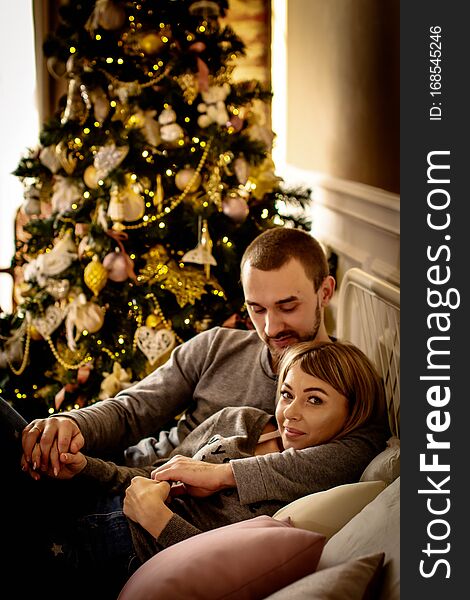 Loving Young Couple Spends Christmas At Home Near A Decorated, Festive Christmas Tree. Man And Woman Are Happy Spending