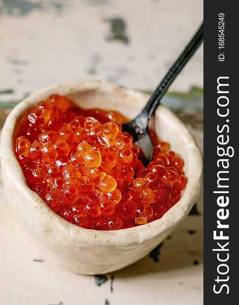 Red salmon caviar in ceramic bowl with spoon on old wooden table. Rustic style, close up. Red salmon caviar in ceramic bowl with spoon on old wooden table. Rustic style, close up