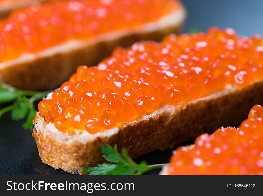 Sandwiches with red caviar on dark stone background, close up