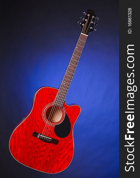 An acoustic electric red wood guitar isolated against a spotlight blue background. An acoustic electric red wood guitar isolated against a spotlight blue background.