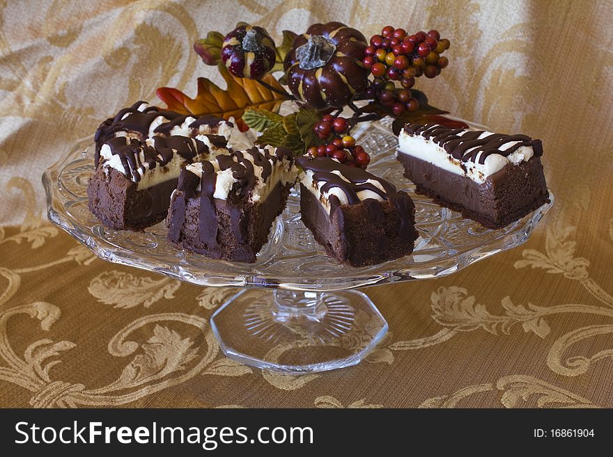 Cheesecake slices on a glass pedestal cake plate on a gold brocade table cloth with autumn greenery decorations