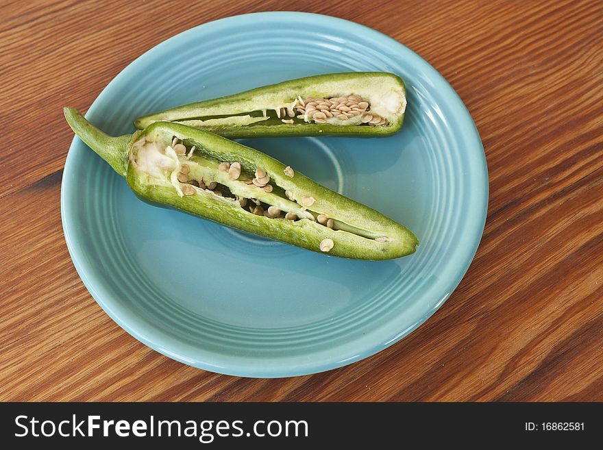 Jalepenos cut in half with seeds showing in a turquioise plate on a wooden table. Jalepenos cut in half with seeds showing in a turquioise plate on a wooden table.
