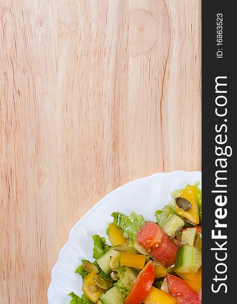 Salad with tomato, pepper, pumpkin seeds on the white plate on the wood table