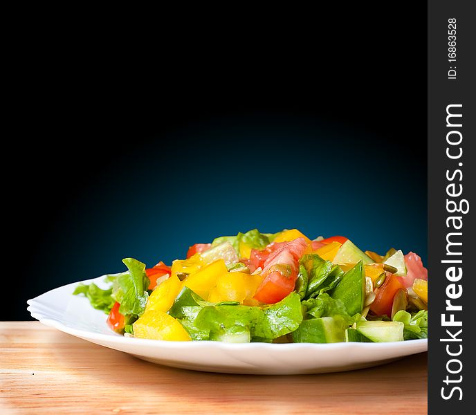 Salad with tomato, pepper, pumpkin seeds on the white plate on the wood table