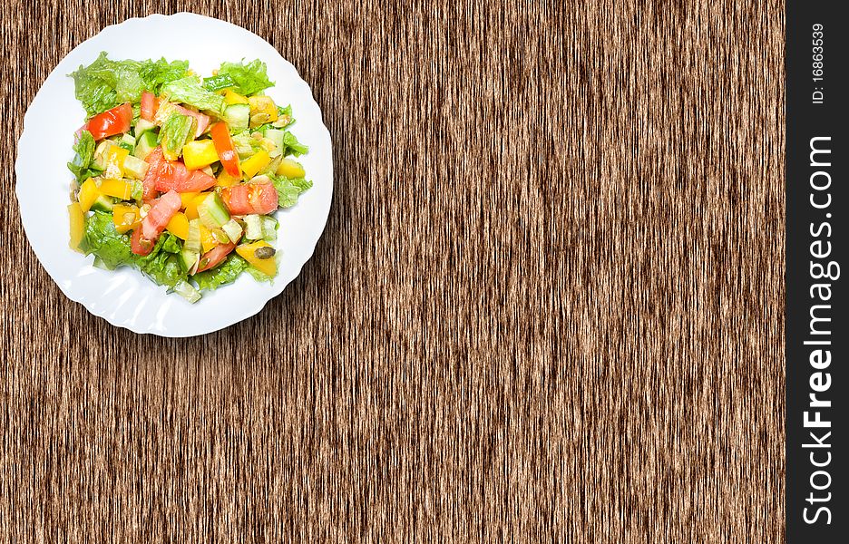 Salad with tomato, pepper, pumpkin seeds on the white plate on the wood table