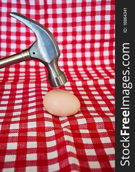 Steel hammer breaking a chicken egg on a striped red background. Steel hammer breaking a chicken egg on a striped red background