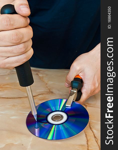 Man destroying a compact disc with a screwdriver. Man destroying a compact disc with a screwdriver