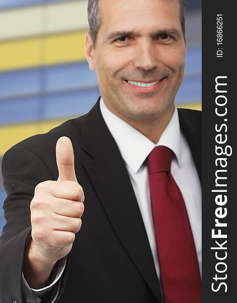 Businessman showing thumbs-up sign - on colourful building background - focus on the hand