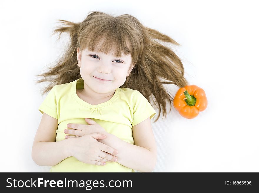 The portrait of a happy little girl lying on the floor with fresh vegetable