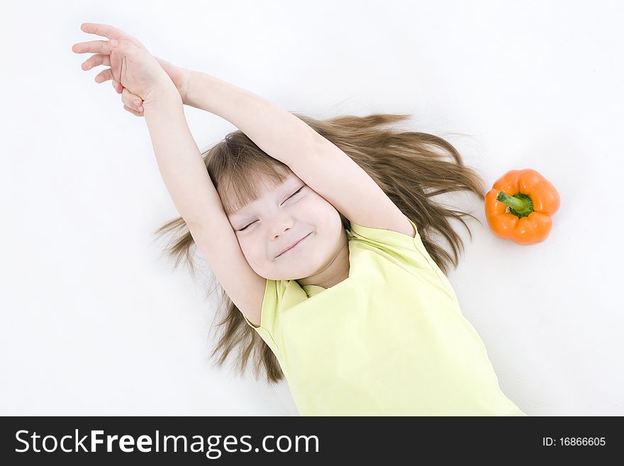 The portrait of a happy little girl lying on the floor with fresh vegetable