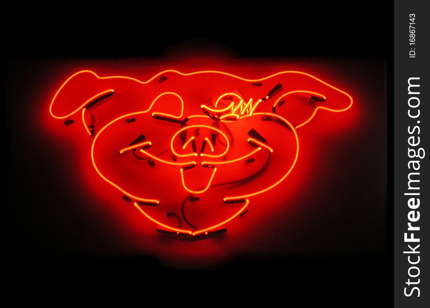 Illuminated, orange glowing pig neon sign for butcher shop on black background at night time. Illuminated, orange glowing pig neon sign for butcher shop on black background at night time