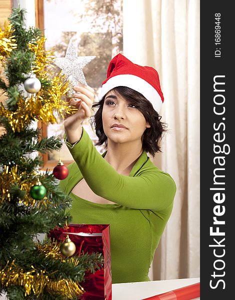 A young brunette with a happy expression getting ready for Christmas by decorating her tree and wearing a Santa Hat. A young brunette with a happy expression getting ready for Christmas by decorating her tree and wearing a Santa Hat.