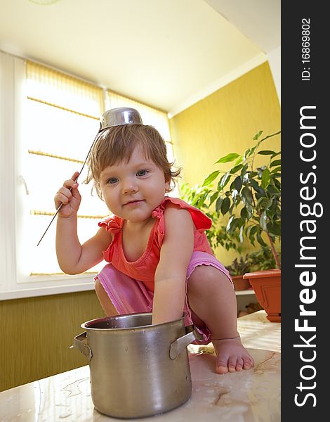 Little girl with a pan and ladle on her head sitting on a table