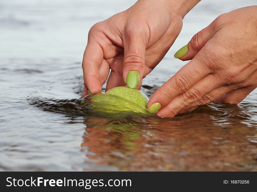 Hands cleaning apple in water.