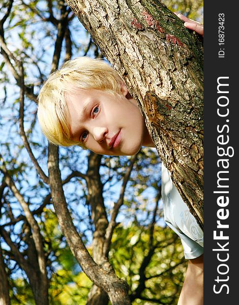 Attractive blond guy behind a tree in park