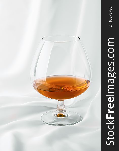 Glass of cognac on white silk. Glass of cognac on white silk