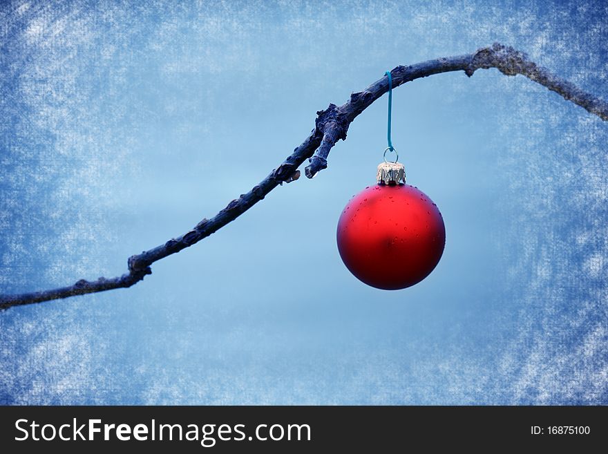 Red ball christmas xmas ornament on a branch in a blue texturized background. Red ball christmas xmas ornament on a branch in a blue texturized background