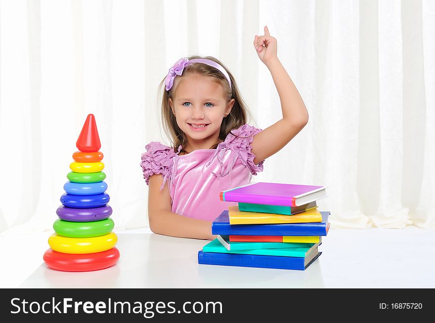 The little girl is studying literature. Reads a book while sitting at a white table.