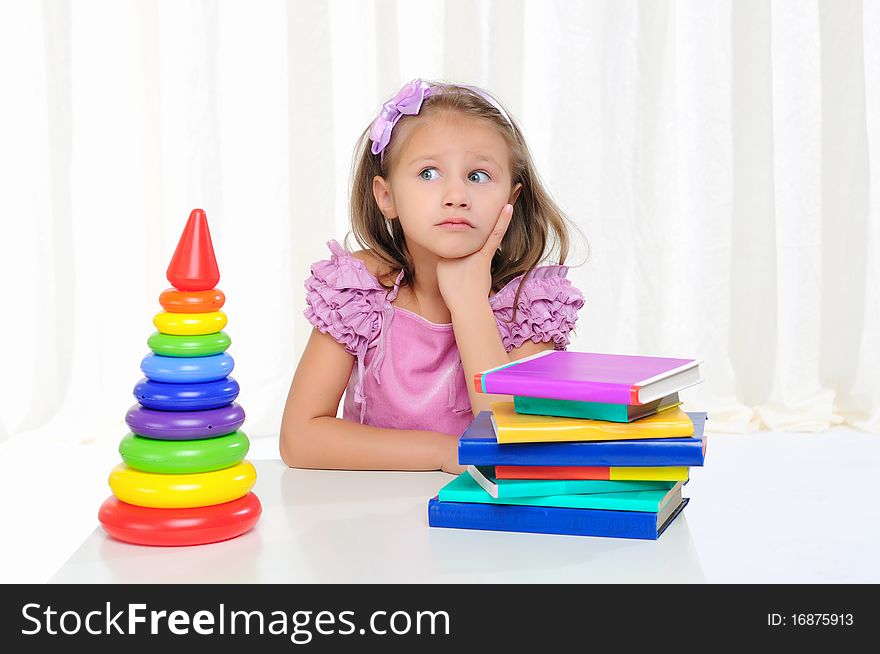 The little girl is studying literature. Reads a book while sitting at a white table.