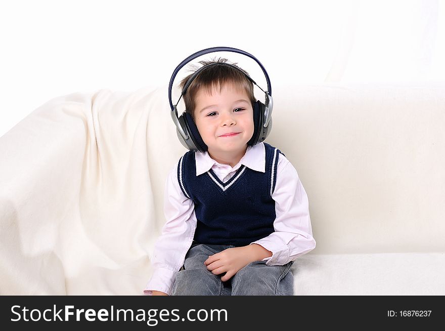 A little boy in headphones enjoys music while sitting on a white sofa. A little boy in headphones enjoys music while sitting on a white sofa