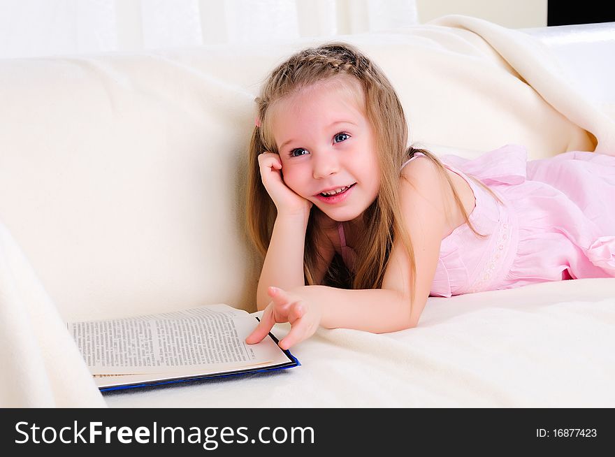 Little girl lying on the couch reading a book