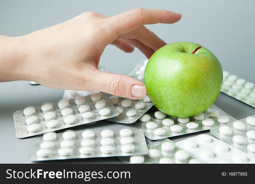 Female hand holds an apple against the scattered tablets. Female hand holds an apple against the scattered tablets