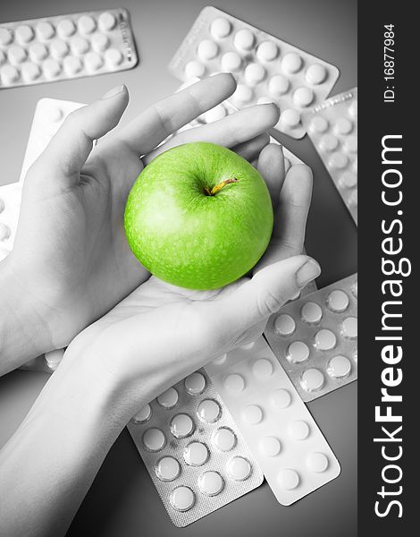 Female hands holds an apple against the scattered tablets. Black-and-white. Female hands holds an apple against the scattered tablets. Black-and-white