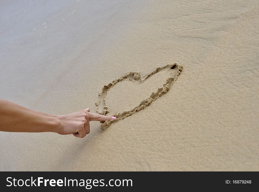 Girls finger is writing heart on the sand