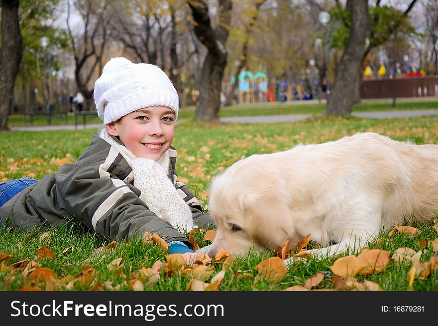 Boy playing in autumn park with a golden retriever.