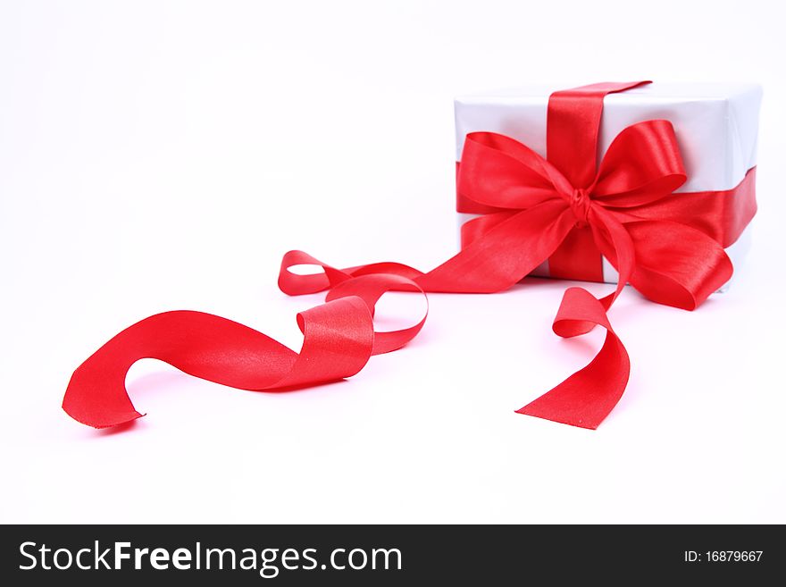 Gift in silver wrapping with a red bow on white background (focus on the ribbon in front). Gift in silver wrapping with a red bow on white background (focus on the ribbon in front)