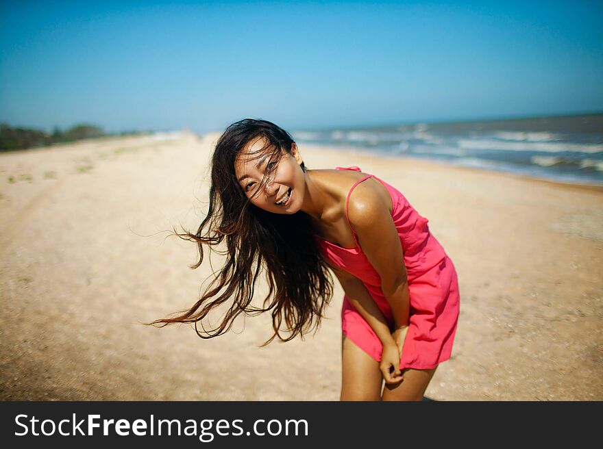 Young asian woman standing at beach. beautiful young woman in a pink dress walking back from the beach.