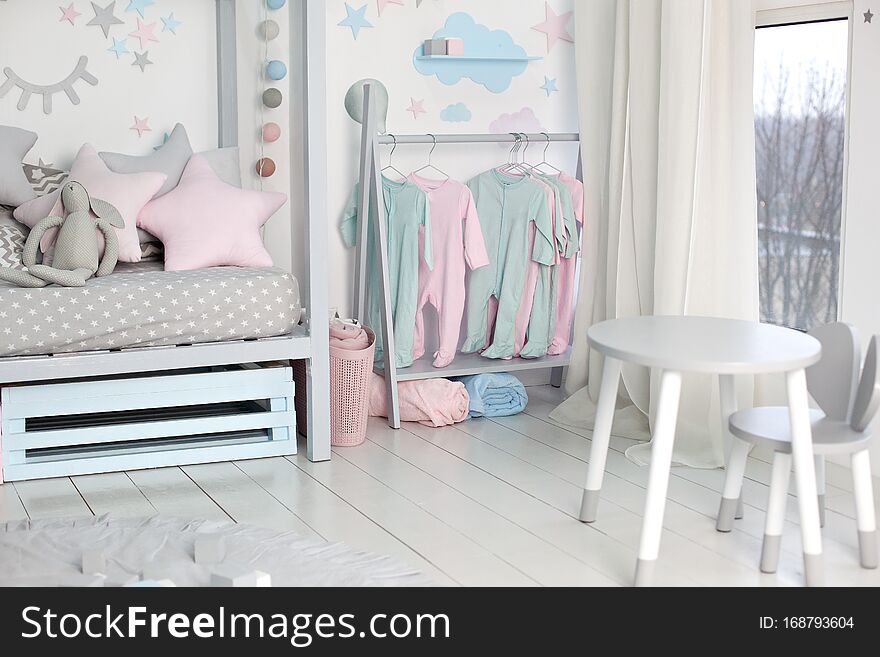 Clothes for little child hung in children room. Rack with hangers with baby clothes. Children cloth rack. Pastel color children clothes in a Row on Open Hanger indoors. Children`s bedroom.  home decor