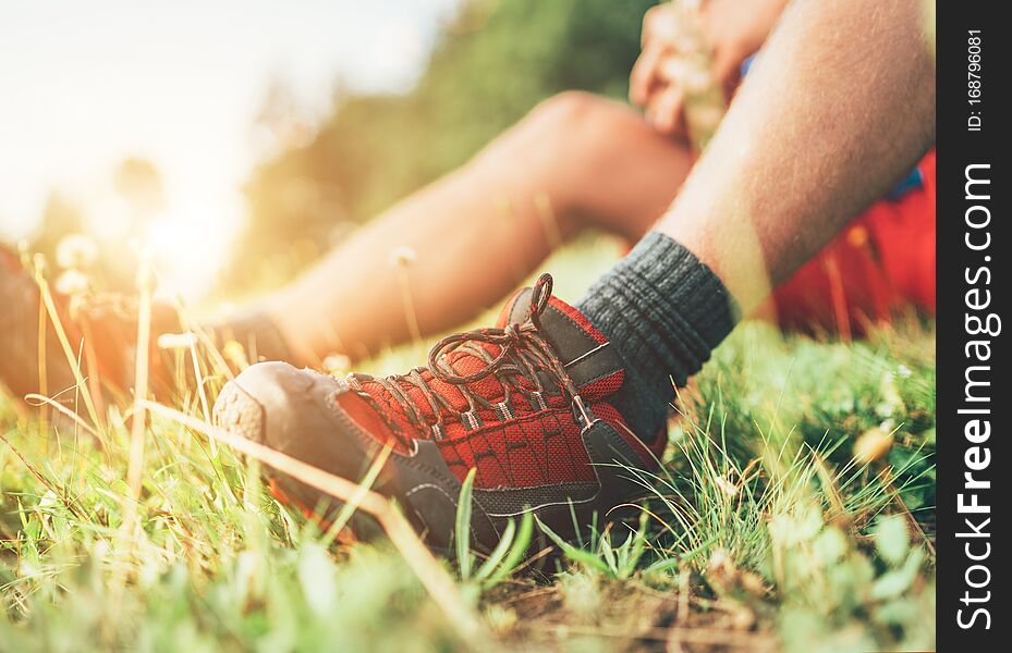 Backpacker`s trekking boots close up shot. Man has a rest break sitting on green grass and enjoying mountain walking, Active