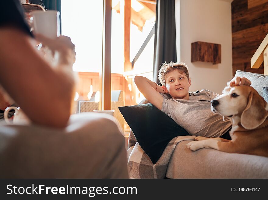 Cozy family tea time. Father and son at the home living room. Boy lying on comfortable sofa and  stroking their beagle dog and smiling. Peaceful family moments concept image