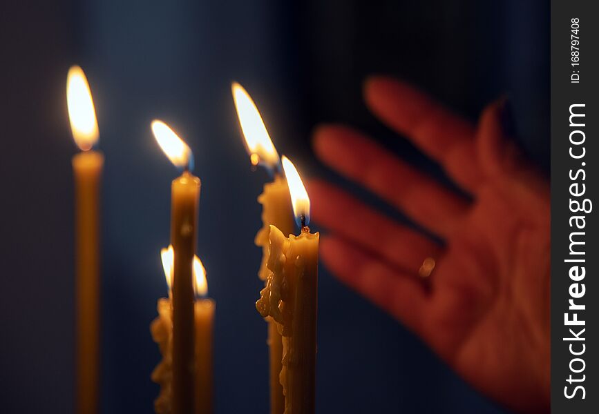 Burning in the dim light of candles in the Christian Church. In the background, a woman`s hand