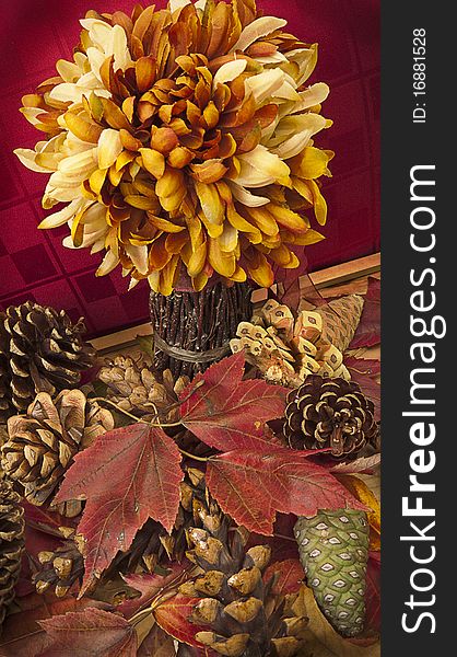 Fall still life with artificial flower arrangement and scattered pine cones and red maple leaves. Thanksgiving decoration. Fall still life with artificial flower arrangement and scattered pine cones and red maple leaves. Thanksgiving decoration.
