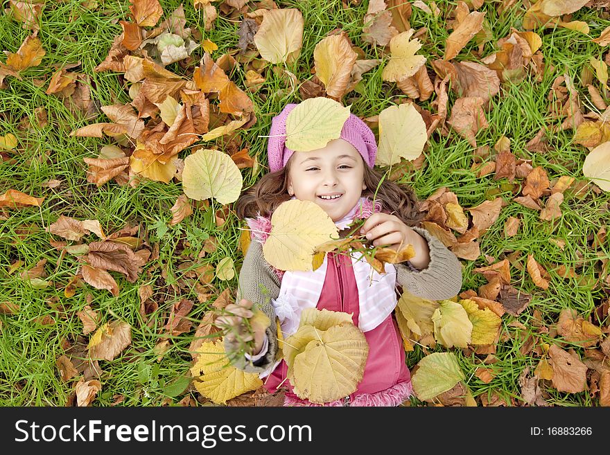 Lying down little girl at grass and leafs in the park. outdoor shot.