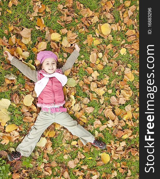 Lying down little girl at grass and leafs in the park. outdoor shot.