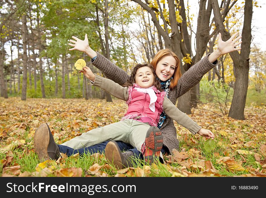 Two sisters sitting on the leafs in the park. Outdoor shot.