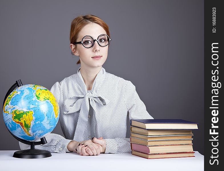 The young teacher in glasses with books and globe. Studio shot.