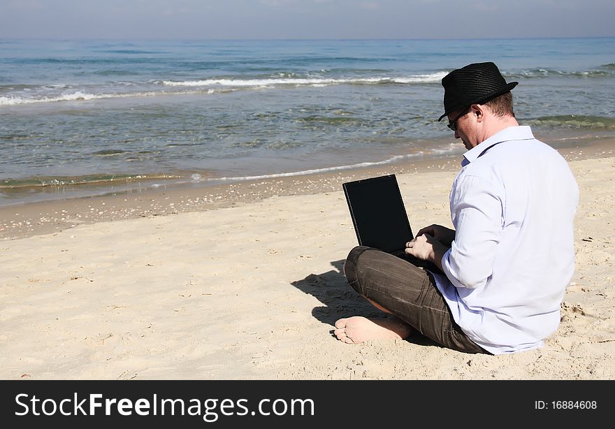 Young man sitting on the beach with laptop