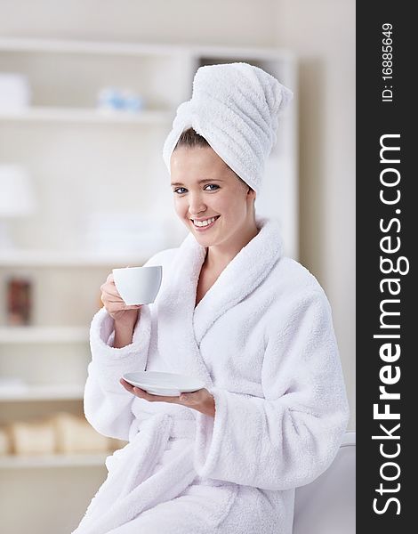 A beautiful young girl in a bathrobe and a towel with a cup of coffee. A beautiful young girl in a bathrobe and a towel with a cup of coffee