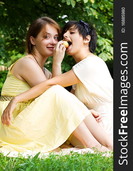 Couple of young attractive chicks sitting on the coverlet in the green park area. Couple of young attractive chicks sitting on the coverlet in the green park area