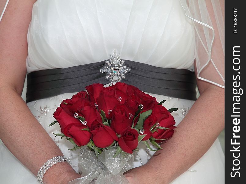 Body of bride holding bridal bouquet of red roses and diamantes.